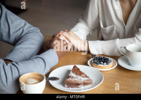 Interracial couple holding hands sitting at cafe table, closeup  Stock Photo