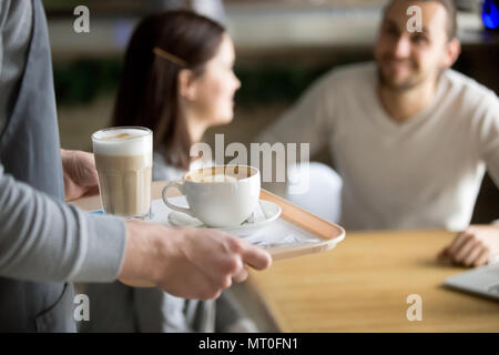 Waitress serving cappuccino and latte to couple in cafe, closeup