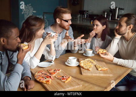 Redhead guy talking to diverse friends eating pizza in pizzeria Stock Photo