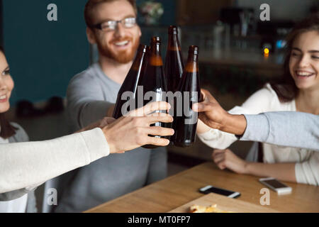 Diverse friends clinking craft beer bottles in pub, cheers conce Stock Photo