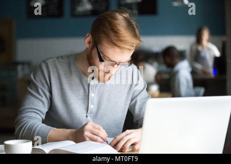 Focused millennial redhead student writing making notes studying Stock Photo