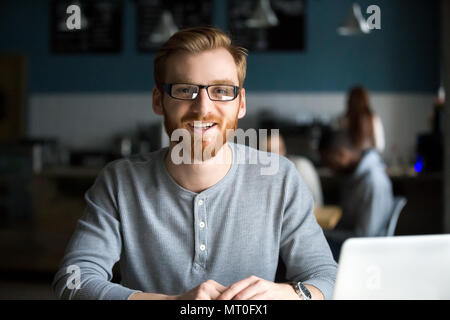 Smiling redhead man with laptop looking at camera in cafe Stock Photo