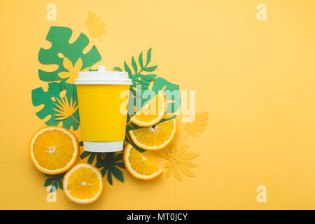 Colorful summer drink concept. Disposable paper cup on a yellow background with tropical leaves and orange slices on a bright yellow background. Stock Photo