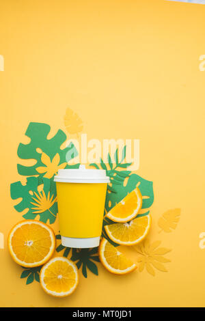 Colorful summer drink concept. Disposable paper cup on a yellow background with tropical leaves and orange slices on a bright yellow background. Stock Photo