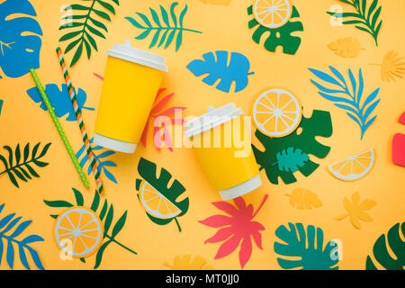 Lemonade paper cups in tropical header with oranges, leaves and fruits pattern on a bright yellow background. Sunny summer colorful flat lay with paper cut outs. Stock Photo