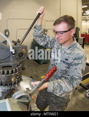 116th Air Control Wing is a Georgia Air National Guard unit operating the E-8C Joint STARS aircraft for airborne command and control missions. The archival image records a maintenance specialist using a rotary punch on sheet metal to fabricate a prototype tablet holder at Robins Air Force Base, Georgia, on July 18, 2017, intended for cockpit use without altering aircraft structure. Stock Photo