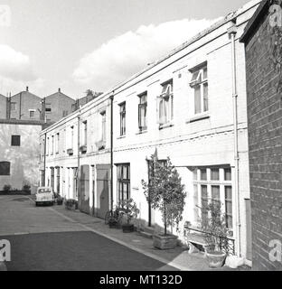 1960s, London, a row of small mews houses. These low-rise, two-storey dwellings were converted from former coach houses or stables and built behind larger city houses in service streets. As the name suggests they were originally built for the horse transport of the wealthy city dwellers. The introduction of the motorcar saw the and of the equestrian usage and in this era they became a fashionable place to live, Stock Photo