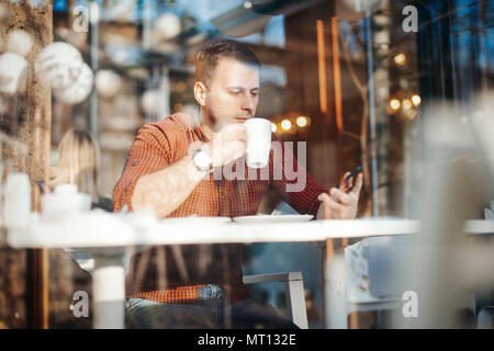 Young attractive man drinking coffee and writing message at mobile phone Stock Photo