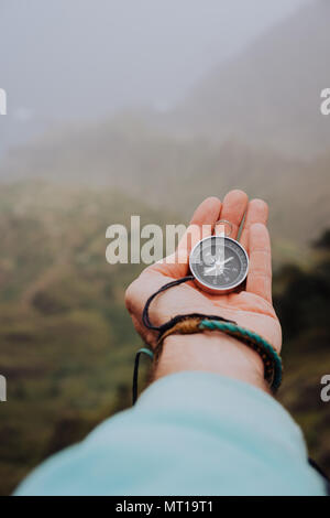 Starched palm with compass. Looking at the compass to figure out right direction. Foggy valley and mountains in background. Santo Antao. Cape Cabo Verde Stock Photo