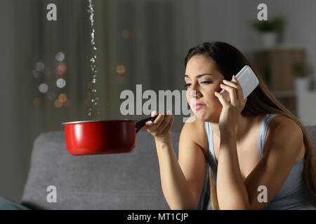 Frustrated girl calling insurance about water leaks sitting on a couch in the living room at home Stock Photo