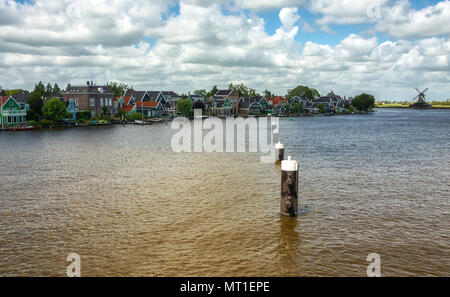 Characteristic green Zaan houses with windmill along the banks of the river Zaan in Zaandijk in the Netherlands Stock Photo