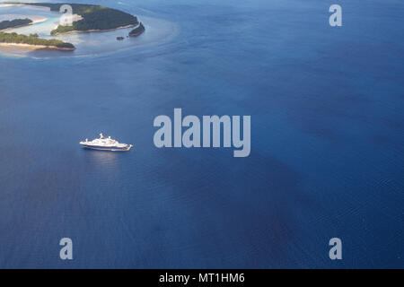 Blue and white mega yacht glides amid tropical islands in pacific waters Stock Photo