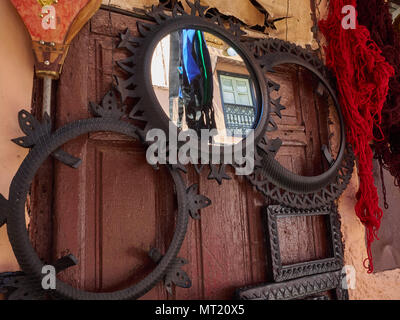 Round mirror in a metal frame on the burgundy wall, next to two empty round metal frames. Stock Photo