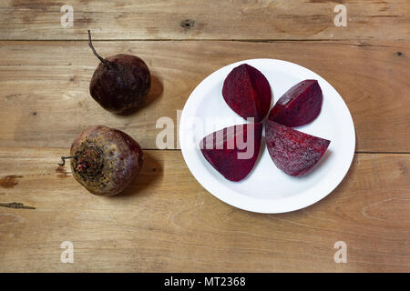 Beetroots, two raw taproots, four steamed slices on white plate, wooden table background, flat lay Stock Photo