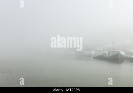 Commercial fishing boats sit tied up to their mooring while blanketed in thick fog in Port Stanley, Canada. Stock Photo