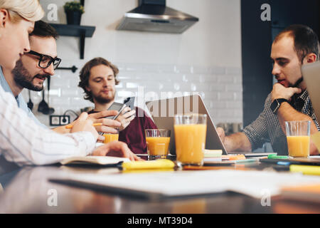 Group of young manager discussing during a meeting. Teamwork on a new startup. Team of businessmen working with electronic gadgets Stock Photo