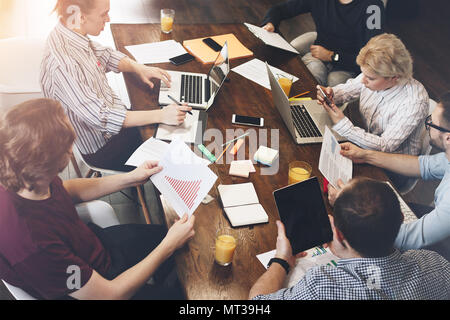 Joint work of young colleagues at a large table with different electronic gadgets and laptops. Discussion of a new startup business team Stock Photo