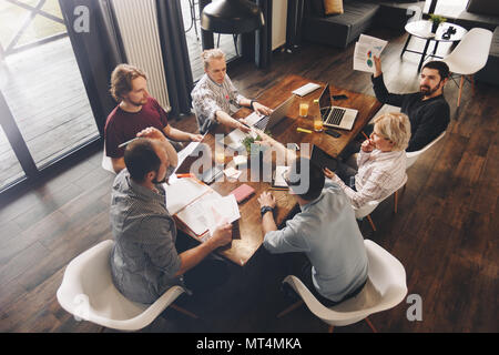 Group of coworking people sitting around wooden table and working on modern laptops in loft. Managers analyze business documents and using touch table Stock Photo