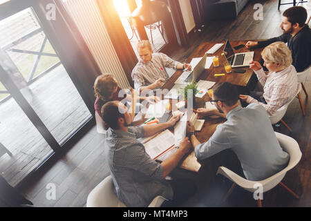 Top view of team of coworkers sitting at wooden table and working with business documents and electronic devices, laptops. Startup diversity teamwork  Stock Photo