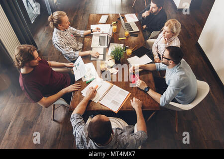 Group of creative managers sits around table. Working process. Teamwork on new project. Coworkers sitting at wooden table and working together on lapt Stock Photo