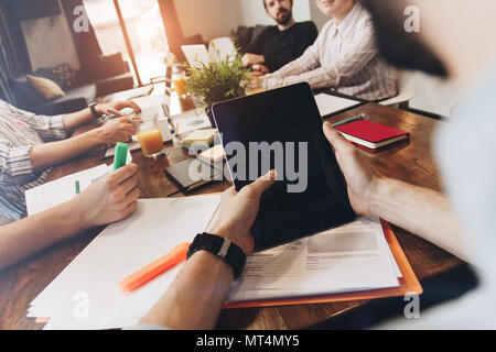 Man holds touch tablet in his hand and discusses with coworkers a new business plan. POV view of male hands holds modern tablet on background of woode Stock Photo