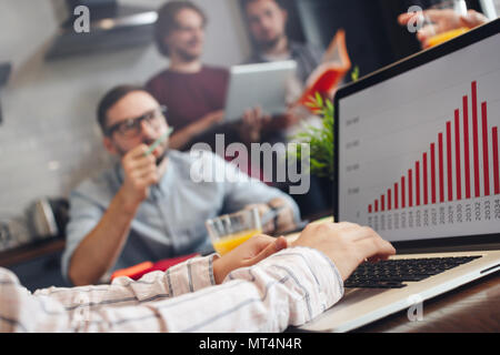 Group of young coworkers or finance analysts discuss about company indicators. Graph and diagram on laptop screen. Teamwork process concept Stock Photo