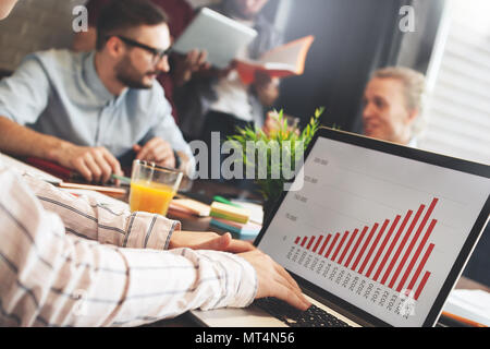 Team of young managers conduct business meeting in loft office. Group of coworkers sitting around wooden table with modern laptop Stock Photo