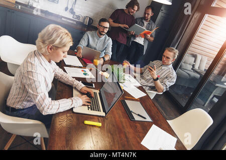 Team of young startup are working on a new project in kitchen. Group of creative businessmen meet together and are working on a new project. Teamwork Stock Photo