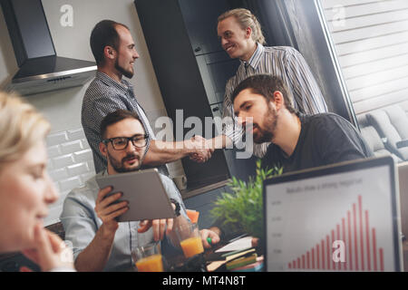 Group of young creative startups are working in kitchen on new project. Meeting partners at home and working together on a new great business. Noteboo Stock Photo