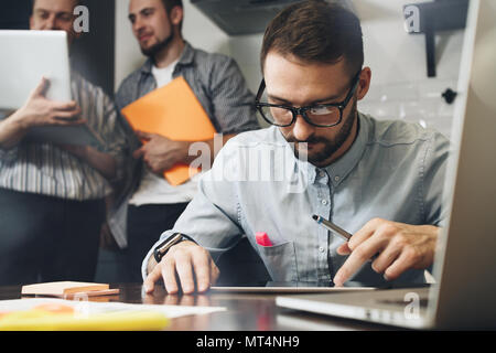 Bearded businessman in glasses uses a computer tablet. Teamwork on a new startup. Business analysts. Coworking in a modern loft space using electronic Stock Photo
