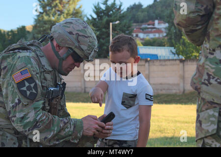 US Army Lt. Col. Mark Himes, commander of the Regimental Engineering Squadron, 2nd Cavalry Regiment, shares his phone with a local Macedonian child during a static display at Stip, Macedonia on July 30, 2017. The 2nd Cavalry Regiment is currently driving by convoy through Macedonia as a part of Dragoon Guardian, an offshoot of Operation Atlantic Resolve, which is a NATO mission involving the US and Europe in a combined effort to strengthen bonds of friendship and to deter aggression. (Photo taken by Pfc. Nicholas Vidro, 7th Mobile Public Affairs Detachment.) Stock Photo