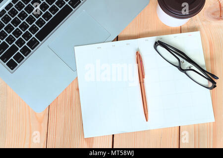 Pen and glasses lay on blank diary book and labtop and coffee cup on wood table,business concept. Stock Photo