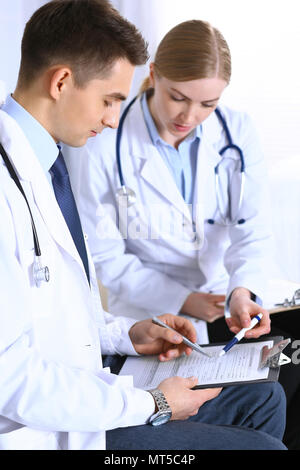 Doctors writing papers using clipboard. Physicians discussing medication program or studying at medical conference. Healthcare, insurance and medicine concept Stock Photo