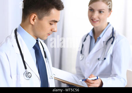 Doctors writing papers using clipboard. Physicians discussing medication program or studying at medical conference. Healthcare, insurance and medicine concept Stock Photo