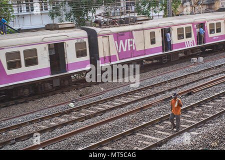 Railway worker walking on the tracks of the local train in Mumbai as a  train passes him by. Stock Photo