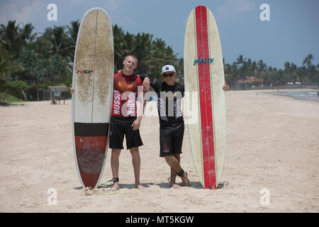 Mirissa/Sri Lanka - April 4, 2018: Two sports men stand on the beach with surfboards. Stock Photo