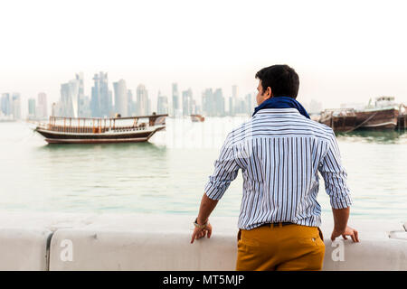Back view of young man outside looking at the view of city buildings and traditional wooden boats at Cor-niche Stock Photo