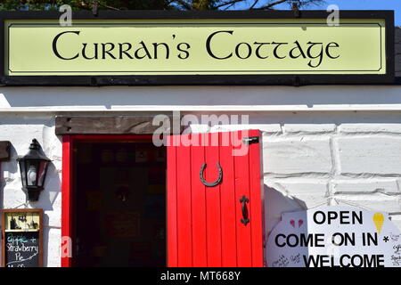 Currans Cottage horizontal detail showing white painted stone wall with red wooden door and large sign above it. Stock Photo