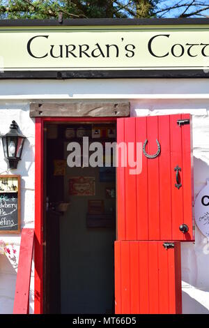 Currans Cottage vertical detail showing white painted stone wall with red wooden door and large sign above it. Stock Photo