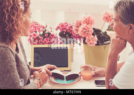couple of friends women middle and third age 40 and 70 year old stay together in happy leisure afternoon eating some cake and drinking fruits. reading Stock Photo