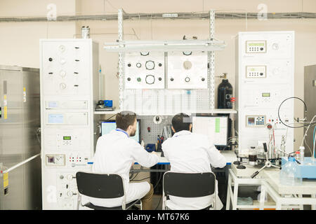 Engineers working with computer connected to control cabinet Stock Photo