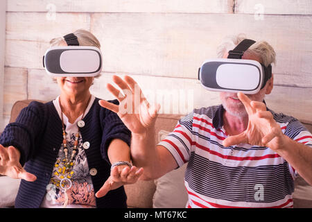 hands to protect while a caucasian man and woman aged 70 years old play at home with internet technology virtual reality goggles headset. smile and la Stock Photo
