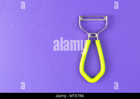 Knife for cleaning vegetables peeler on mauve background. Knife for legumes peeling on mauve background. Green peeling, useful as food presentation. Stock Photo