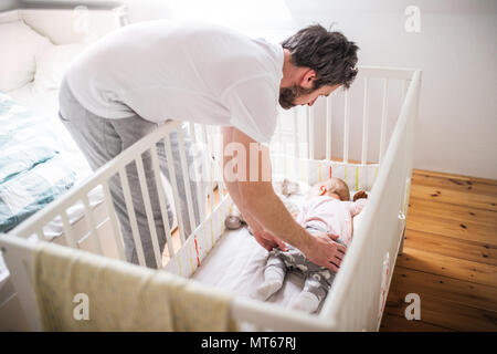 Father putting a sleeping toddler girl into cot at home. Stock Photo