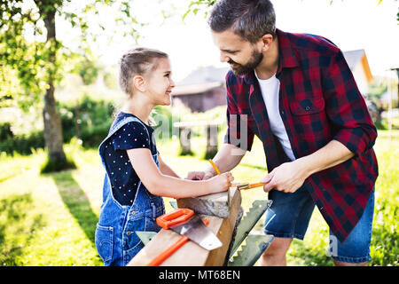 Father with a small daughter outside, making wooden birdhouse. Stock Photo