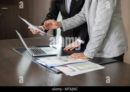 Asian businesswomen holding a pen and analysis documents on office table with laptop computer and graph financial diagram working in the background Stock Photo