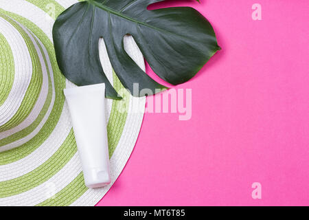 on green monstera leaf with sunglasses and straw hat on pink marble table Stock Photo