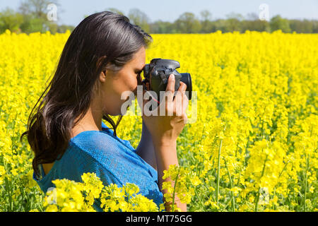 Young colombian woman with camera taking photo of yellow rapeseed field Stock Photo