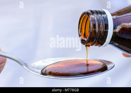 Hand pouring medication or antipyretic syrup from bottle to spoon. healthcare, people and medicine concept. Stock Photo