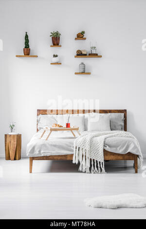 Front view of a wooden framed double bed with linen, pillows and blanket in a contemporary bedroom interior of a hotel. Food tray with breakfast stand Stock Photo